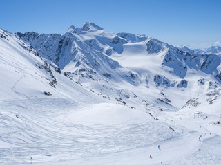 Fototapeta na wymiar Winter landscape with snow covered mountain slopes and pistes with skiers enjoying spring sunny day at ski resort Stubai Gletscher, Stubaital, Tyrol, Austrian Alps