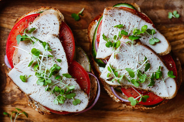 Sandwiches with turkey meat and fresh vegetables served with microgreens on a wooden plate. Top view, flat lay, macro food photography.