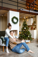 Happy couple, husband and wife are sitting near a decorated Christmas tree on Christmas Eve. New Year and Christmas holidays