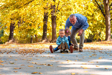Grandchildren having fun with grandfather in the autumn park while riding skateboard