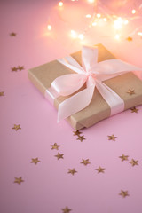 Gift in craft paper with a pink bow on a pink background with holographic sparkles in the form of stars. Template  banner for greeting card your text design 2020. New year, christmas, birthday