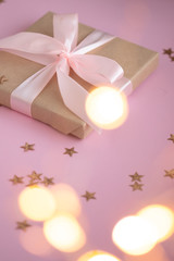 Gift in craft paper with a pink bow on a pink background with holographic sparkles in the form of stars. Template  banner for greeting card your text design 2020. New year, christmas, birthday
