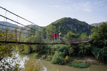 two lovers walking on a narrow steel bridge over a river at nature
