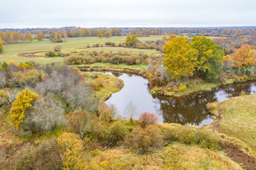 Forest in autumn colors. Colored trees and a meandering blue river. Red, yellow, orange, green deciduous trees in fall. Peetri river, Estonia, Europe