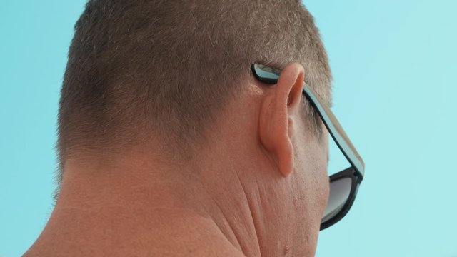 Back view of man in sunglasses against blue sky. Close-up partial view of male head on blue sky background at sunny summer day