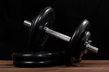 Fototapeta na wymiar Big black male dumbbell on a brown wooden table on a black background