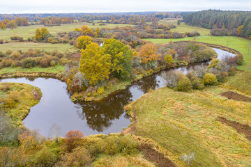 Fototapeta na wymiar Forest in autumn colors. Colored trees and a meandering blue river. Red, yellow, orange, green deciduous trees in fall. Peetri river, Estonia, Europe