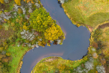 Forest in autumn colors. Colored trees and a meandering blue river. Red, yellow, orange, green deciduous trees in fall. Peetri river, Estonia, Europe