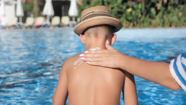 Caring mother hand applying sunblock lotion on tanned back child skin during sunbathing
