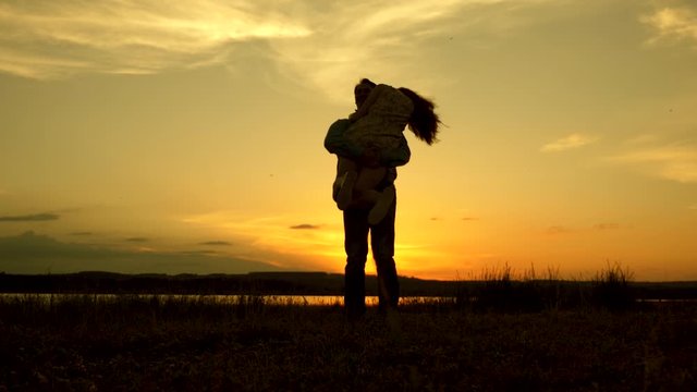 Loving man and woman dance in bright rays of sun on the background of lake. Young couple dancing at sunset on beach. Happy guy and girl waltz in the evening in the summer park.