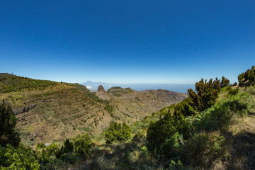 Panoramic view of Tenerife Island with volcano Teide above horizon and Los Roques peaks near Garajonay national park at La Gomera. Thickets of relic laurels and heather on steep green slopes. Canary