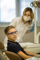 Teenage boy patient sitting in a chair and woman dentist, together portrait in dental room.