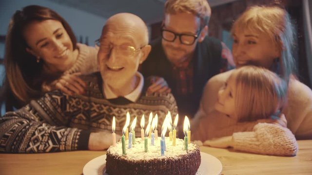 Senior man blowing candles on cake celebrating birthday with family