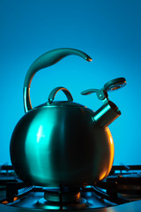 Photo of stainless steel kettle in neon light over blue background.