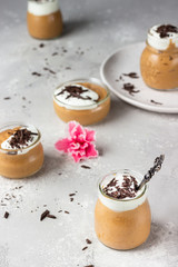 Chocolate mousse with whipped cream and pieces of chocolate in portion glasses, light grey background. Copy space.