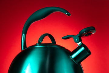 Close-up photo of stainless steel kettle in neon light over red background.