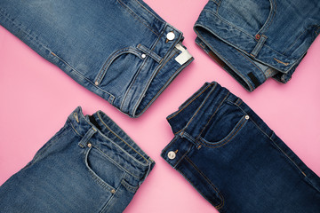 Several pairs of blue denim jeans on pink background
