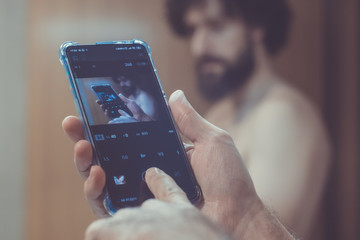 Bearded, caucasian, middle aged and naked male manipulating his smartphone
