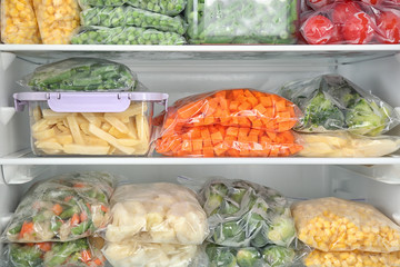 Plastic bags and containers with different frozen vegetables in refrigerator