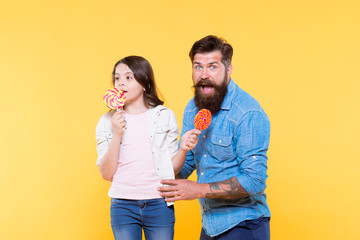 candy shop. happy childhood. Daughter and dad eat candy. bearded hipster man is good father. little girl and dad hold colorful lollipop. summer vibes. happy family. cheerful about dessert