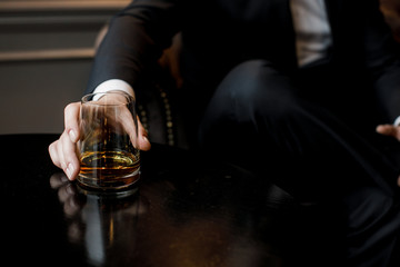 man in a suit holds a glass with whiskey