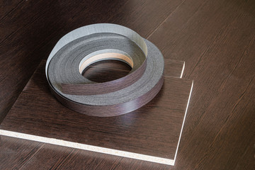 Edging tape lying on laminated chipboard sheets wenge color. Roll melamine edge for finishing of...