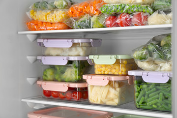 Plastic bags and containers with different frozen vegetables in refrigerator