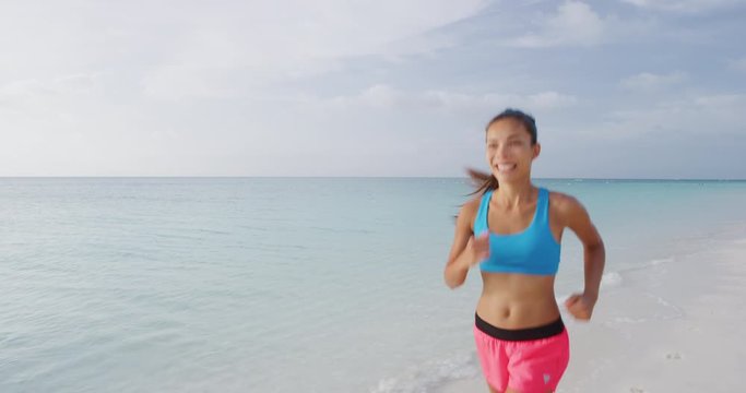 Young woman athlete running on beach exercising. Female runner sprinting training at the ocean smiling happy.