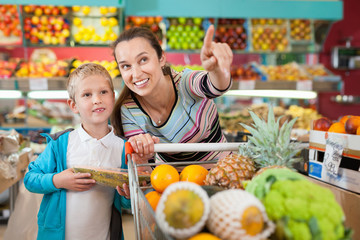 Portrait of happy woman and her little son with shopping cart full of fruits and vegetables