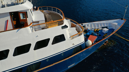 Aerial drone bird's eye top view photo of luxury yacht with wooden deck docked in deep blue waters, Cyclades, Greece