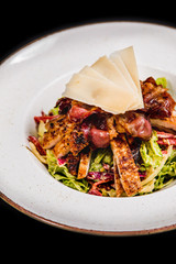 Meal made of green salad,  fresh chicken, crispy bacon nad cheese on top