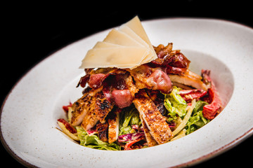 Meal made of green salad,  fresh chicken, crispy bacon nad cheese on top