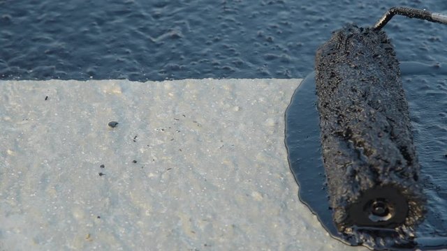 Waterproofing coating. Worker applies bitumen mastic on the foundation. Roofer cover the rooftop polymer modified bitumen waterproofing primer, with a roller brush.