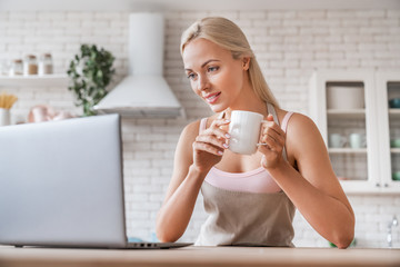 Woman with cup of coffee and laptop in the kitchen