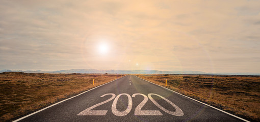 The word 2020 written on highway road in the middle of empty asphalt road at golden sunset and beautiful blue sky. 