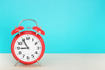 Red retro alarm clock with five minutes to nine o'clock, on wooden table on a blue background. The concept of time, holiday, 5 minutes to the event, deadline. Layout with copy space for your text.