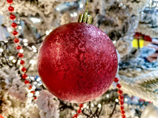 Red ball ornament hanging on a holiday christmas tree as home decoration for festive new year eve with snowy pine tree