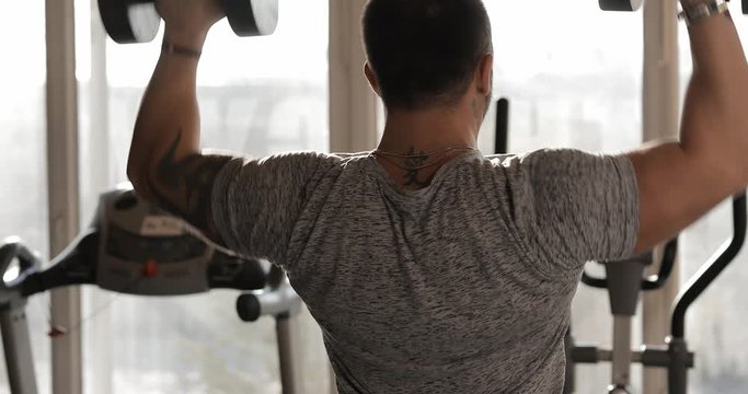 Man lifting dumbbells in a gym making exercise for deltoid muscles, back view