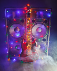 electric guitar with festive Christmas lights and music speakers in smoke