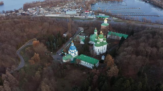 Quadrocopter flight over Vydubychi monastery with copper green roof, church bell towers and gold domes. Vydubychi Monastery with its main temple, refectory and bell tower among the trees in autumn.