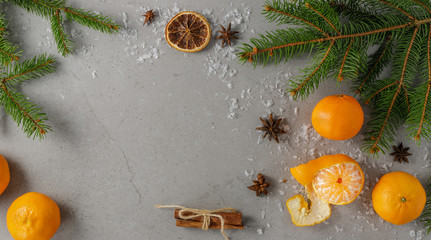 Winter Christmas festive decoration on a stone grey board with five fresh mandarins, fir branches, anise, cinnamon and artificial snowflakes. With space for text, top view