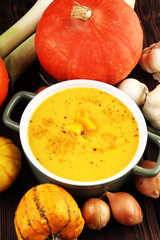 Roasted pumpkin and carrot soup with cream and pumpkin seeds on rustic background.