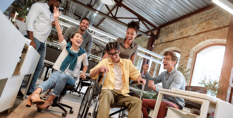 Does work make you happy. Young positive asian man in wheelchair having fun with his colleagues at...