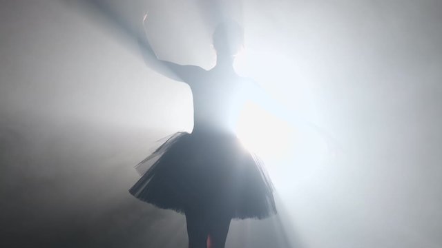 Silhouette of incredible girl dancing ballet in tutu on stage front of spotlight