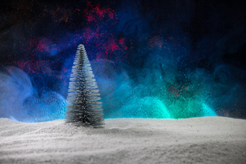 Fir tree standing on snow with beautiful holiday decorated background and traditional holiday attributes.