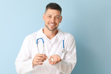 Doctor with pills on color background