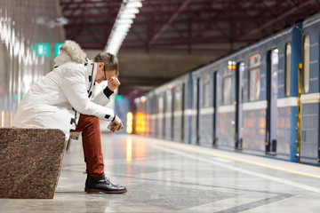 Crying man in white parka very upset, holding smartphone, gets bad news, holds forehead with his...