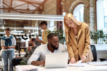 Together we can achieve more. Young afro american cheerful man discussing new project with his beautiful female colleague while working together in the modern office