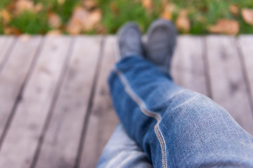 Sit on the bench. Look down at your feet. Sitting in jeans in the park.