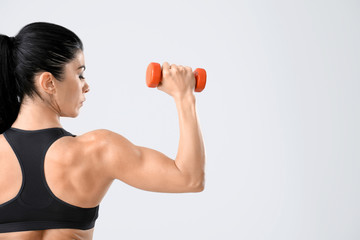 Sporty muscular woman with dumbbell on light background